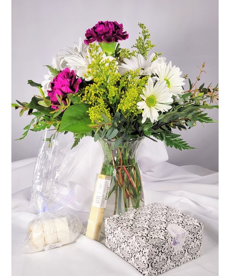Hot pink carnations, yellow daisies & purple statice arranged in glass vase. Paired with a box Pralines of Prescott Chocolates a bath bomb & Teaspressa flavored sugar cubes. 