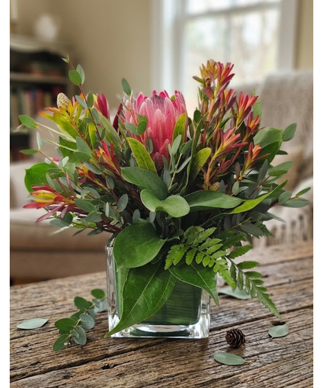 Wooden box with lush greenery, sunset leucadendron and a pink mink protea