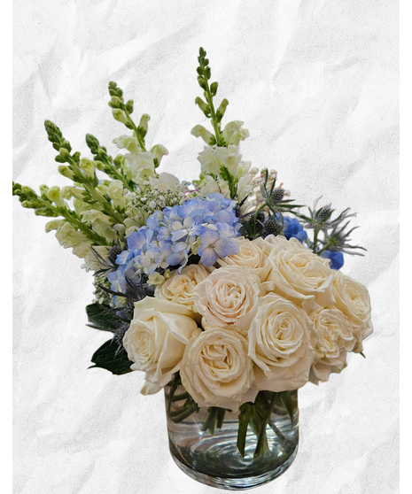 White roses, blue hydrangea, stock and eryngium in a clear glass vase